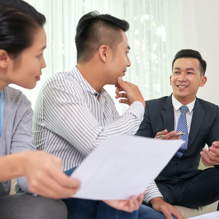 Smiling Vietnamese real estate broker consulting young couple at meeting