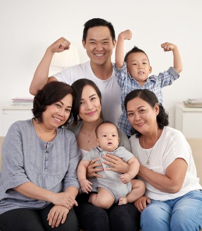 Portrait of big Asian family posing for photo at home: sitting on sofa, looking at camera and smiling happily
